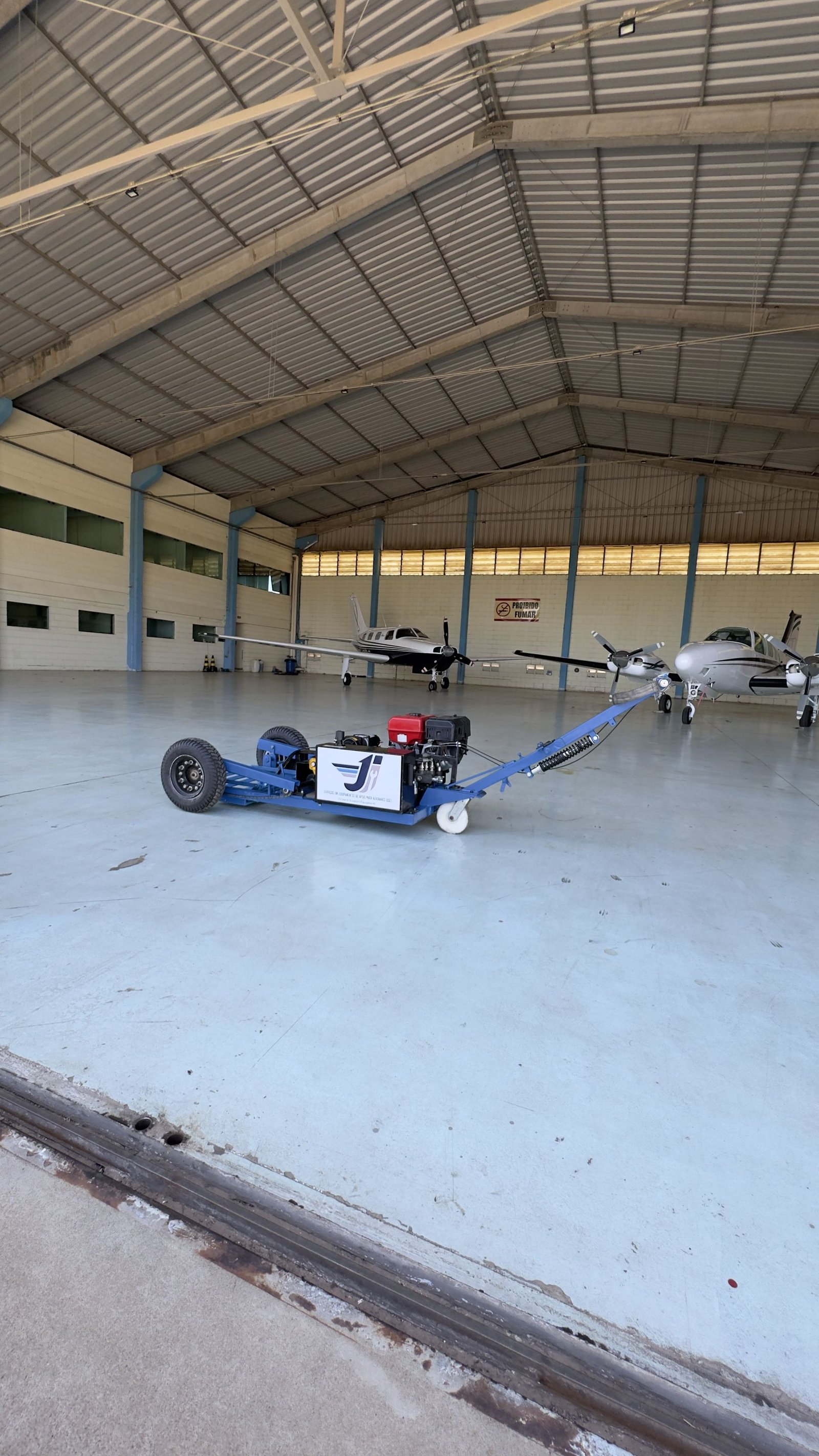 Rebocador JI em pátio de hangar, ao lado de aeronaves de pequeno e médio porte