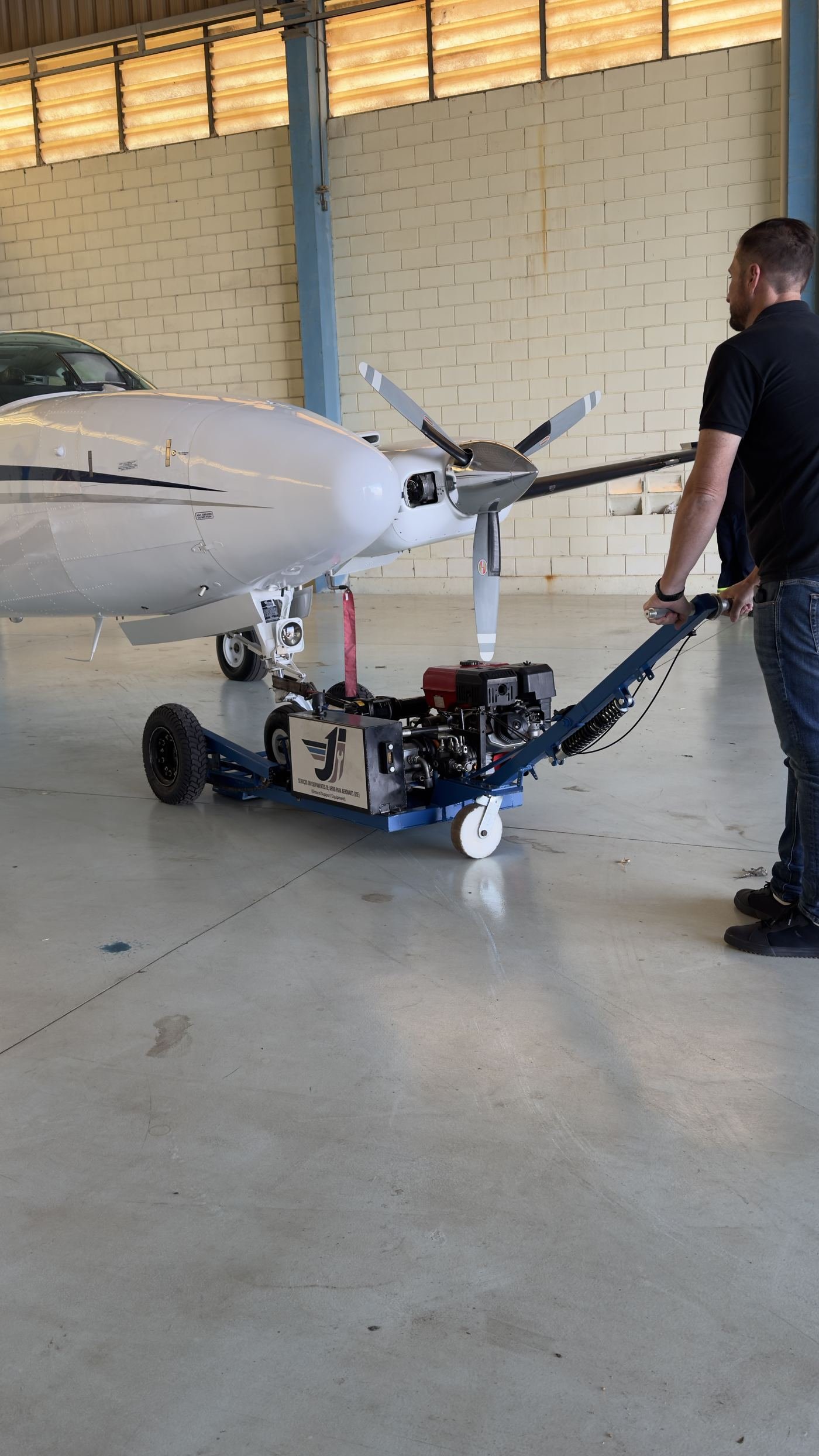 Rebocador de pushback JI movimentando aeronave bimotor dentro de hangar